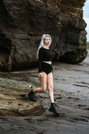 Slender woman wearing fitted black yoga crop top and black yoga shorts.