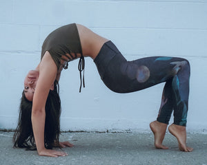 5 foot 7 inches woman in a back bend position wearing and earthy green khaki colored top and dark leggings with a watercolor full moon pattern on the left leg
